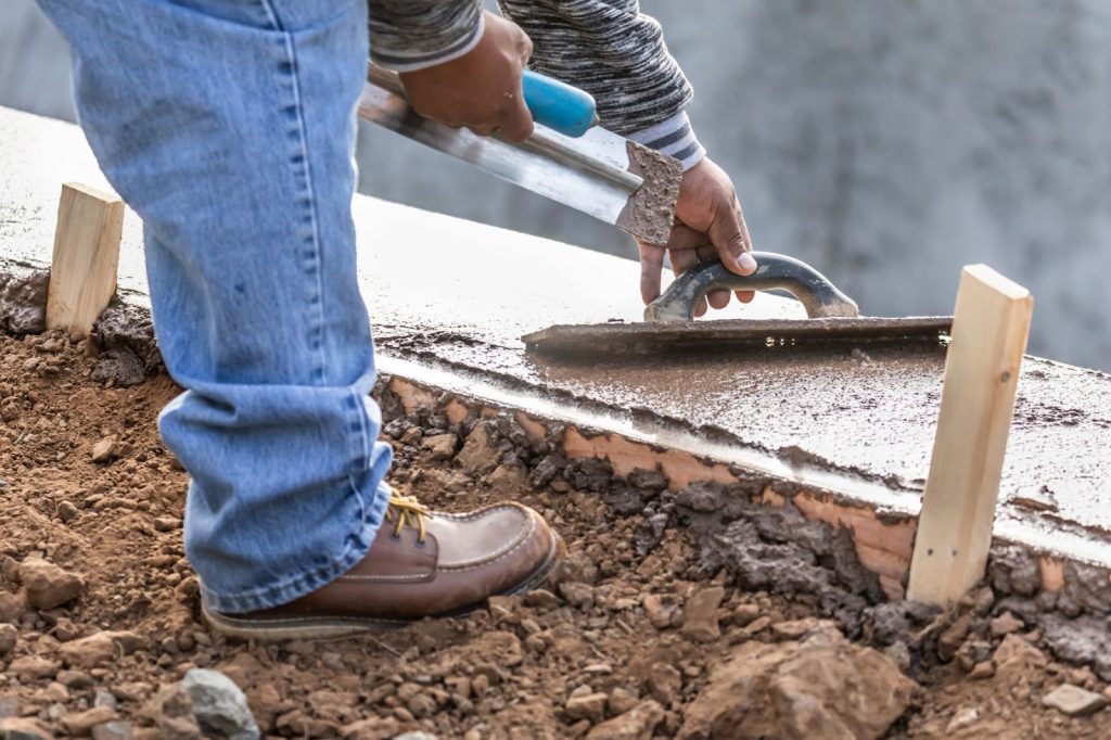 A man leveling the concrete outside next to the gravel.