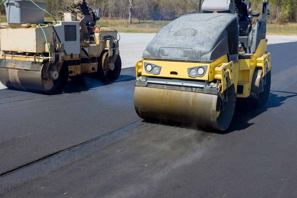 A worker operates a road roller compactor to lay new asphalt.