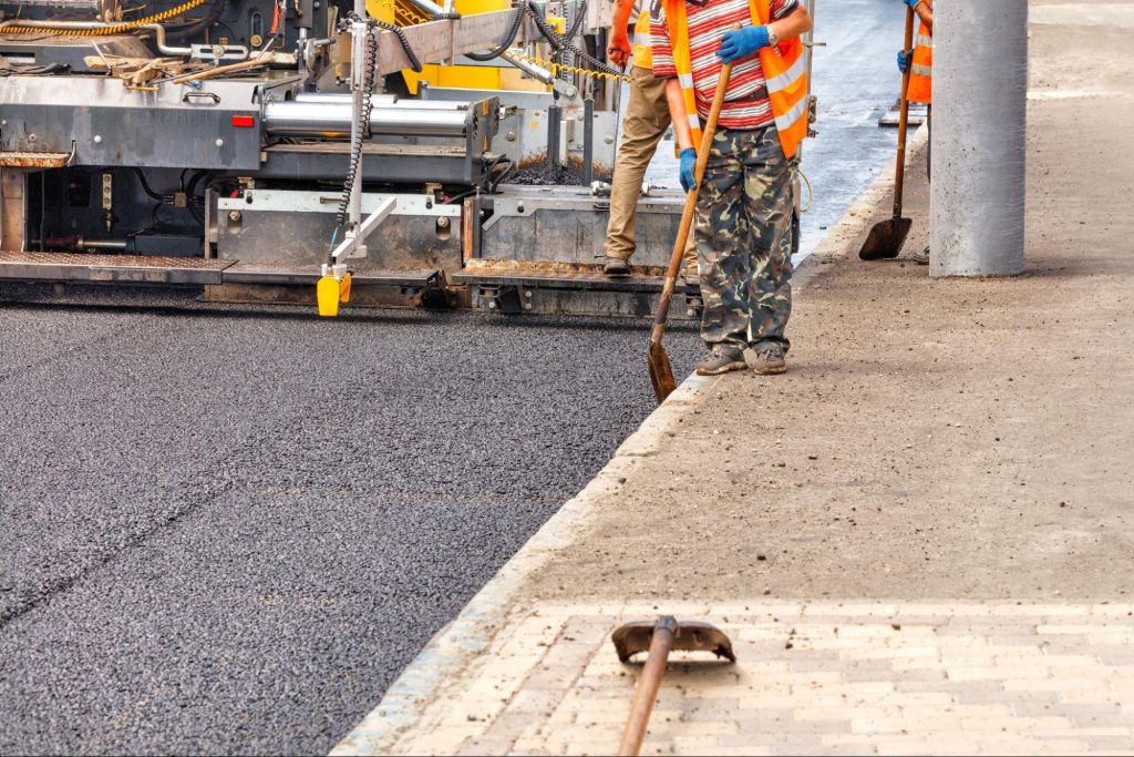 Construction workers paving concrete next to a sidewalk. 