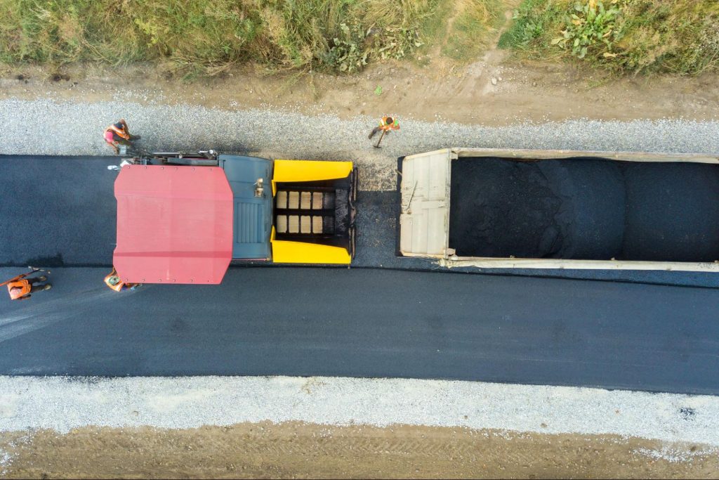 An aerial view of new road construction with asphalt paving machinery in operation.
