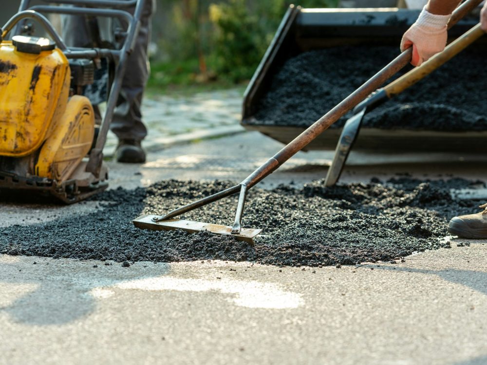 Low angle view of two workers arranging fresh asphalt mix with rakes and shovel
